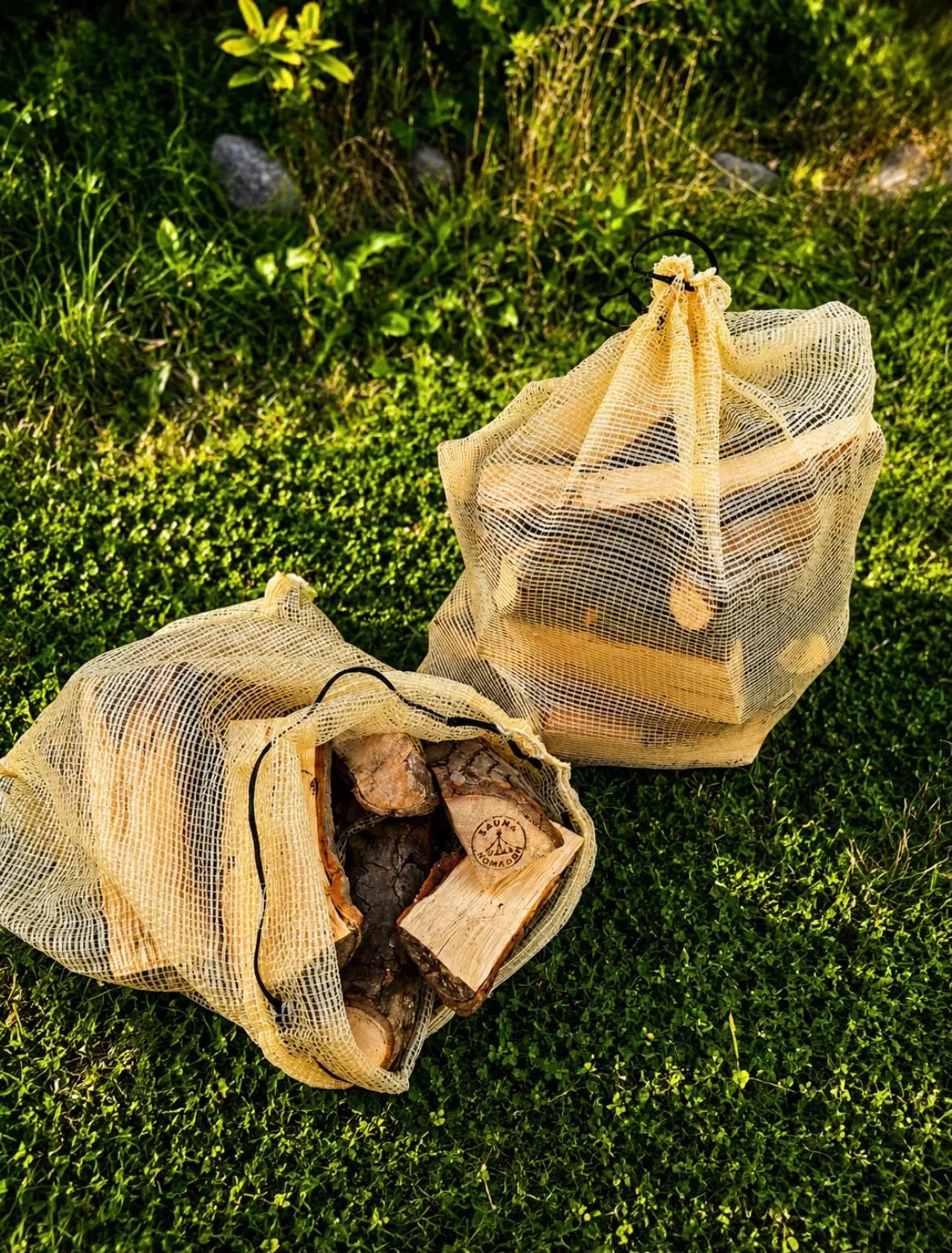 Zwei mit Brennholz gefüllte Netzsäcke auf dem Rasen im Sonnenlicht