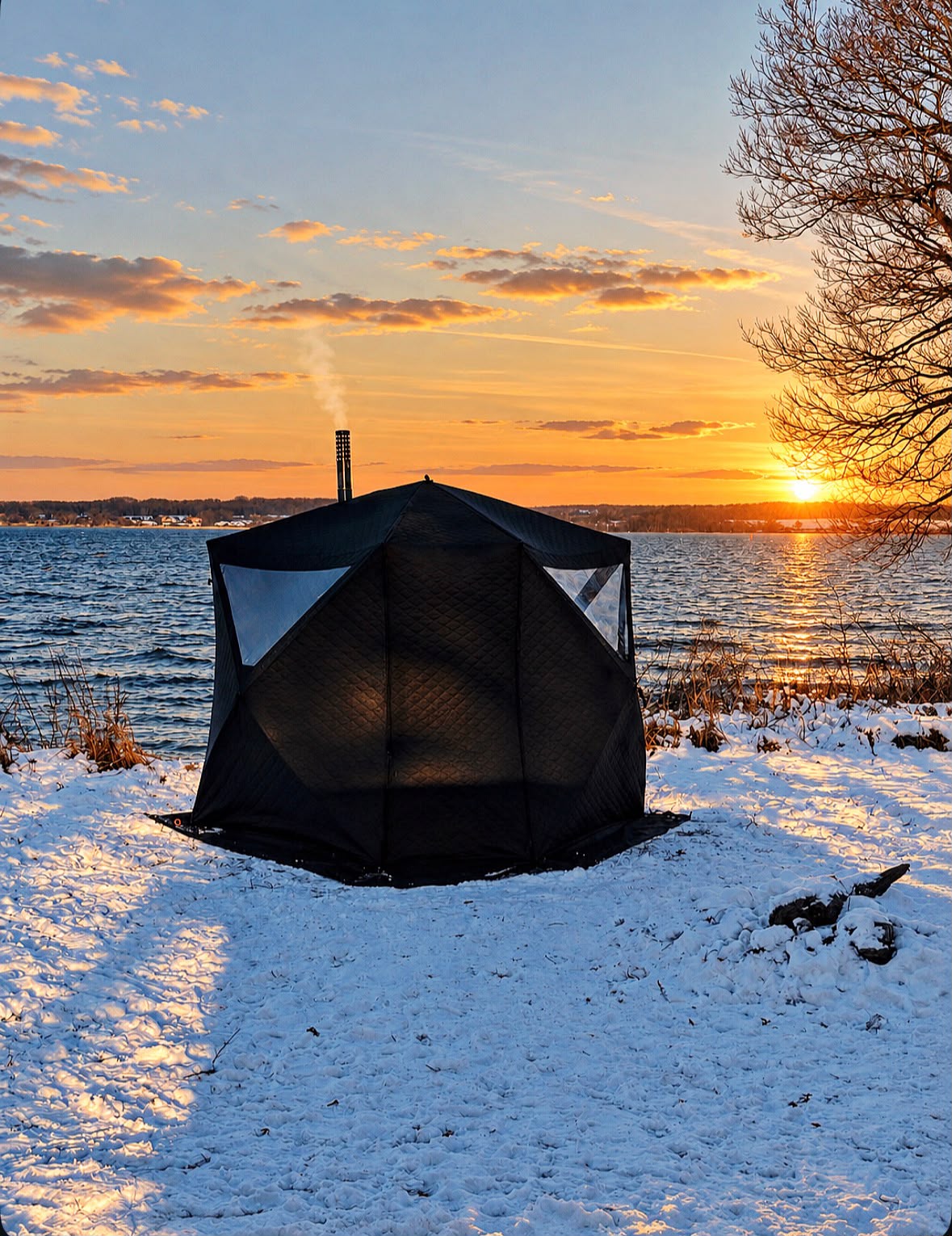 Zeltsauna im Schnee am See bei Sonnenuntergang, Rauch steigt aus dem Schornstein